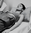 Black and white photo of a person lying in bed with pillows and blankets.