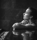 Black and white photo of a woman sitting by a pool with a dark background