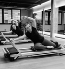 Two women exercising on Pilates reformers in a studio setting.