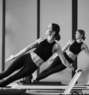 Woman exercising on a Pilates reformer machine in a studio setting.