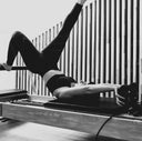 Person exercising on a Pilates reformer machine in a studio setting.